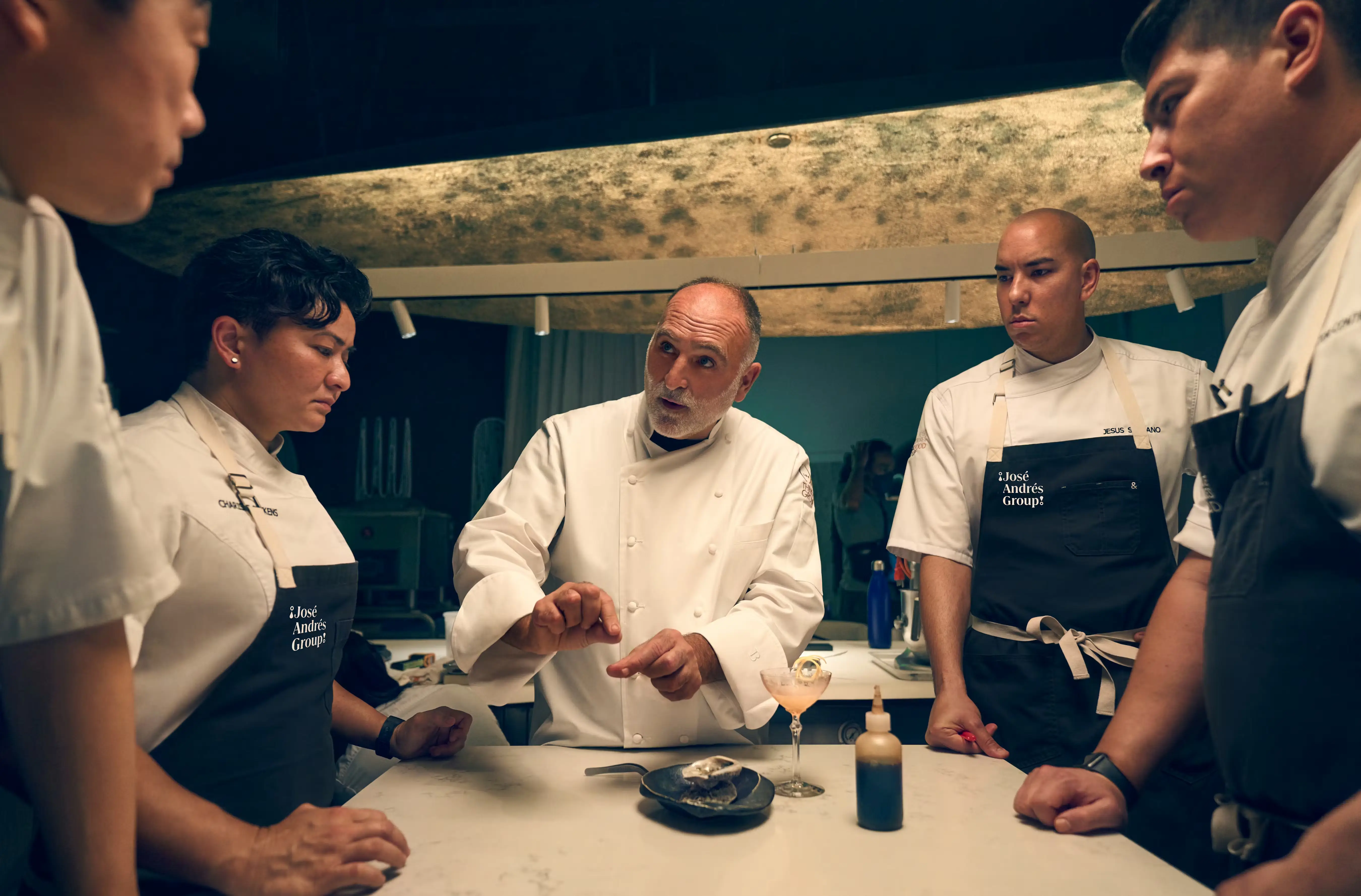 employees standing around a table in a restuarant listening to a chef